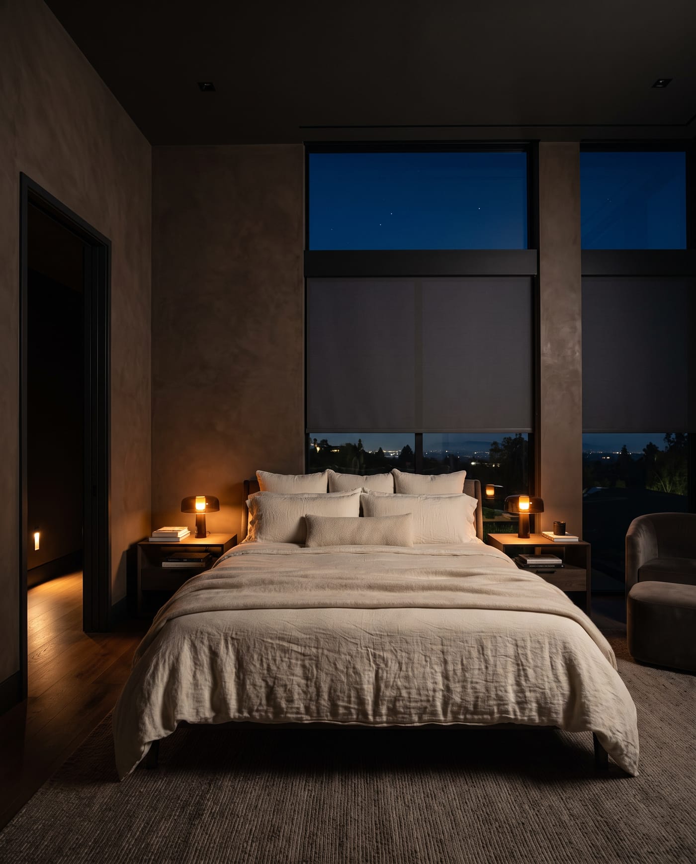 The principal bedroom at night, shades lowered, two low amber lamps